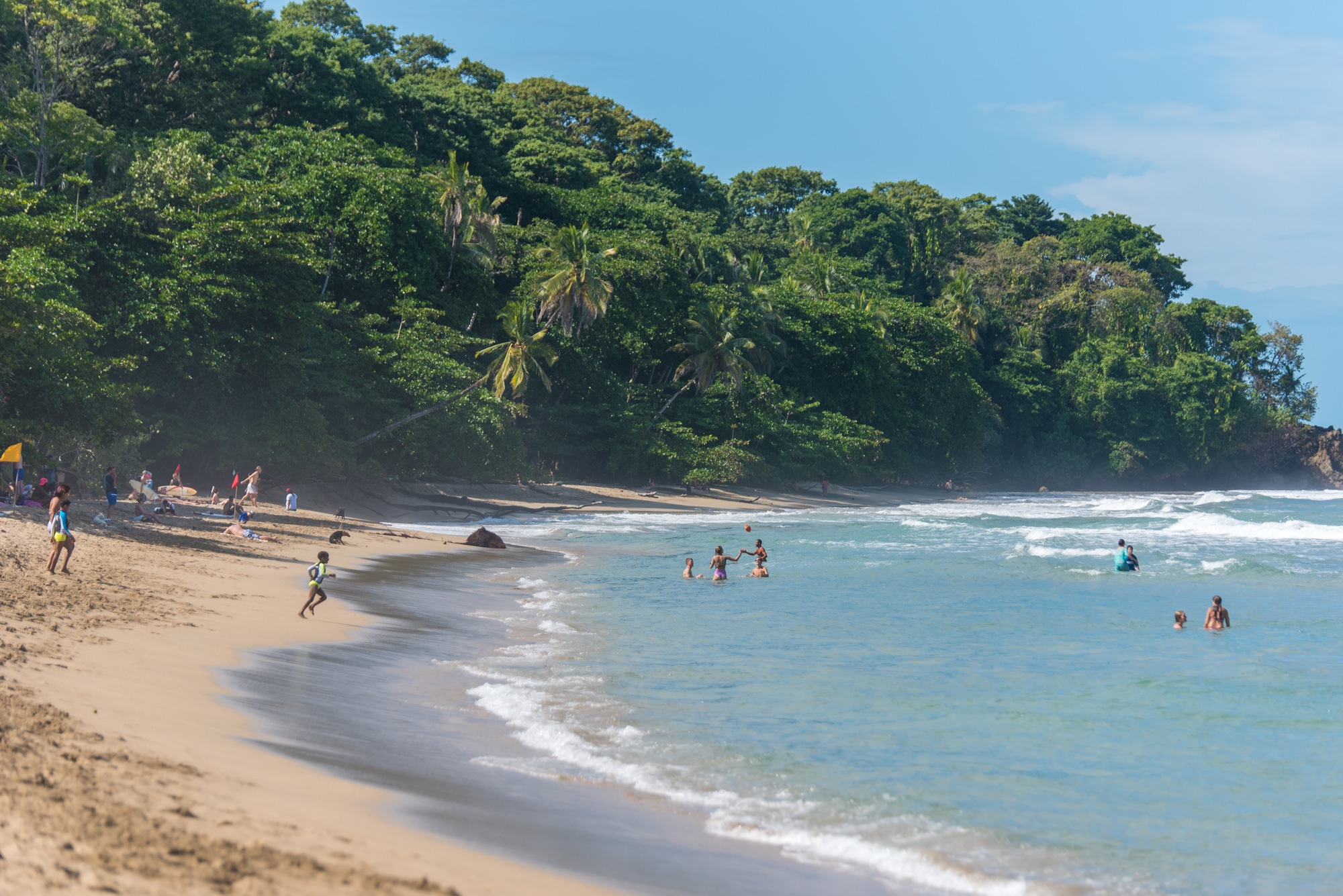 Playa Cocles beach with swimmers, sand, and lush greenery. 