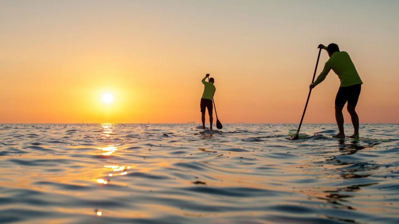 Two people paddleboarding on ocean at sunset, calm scenic view.