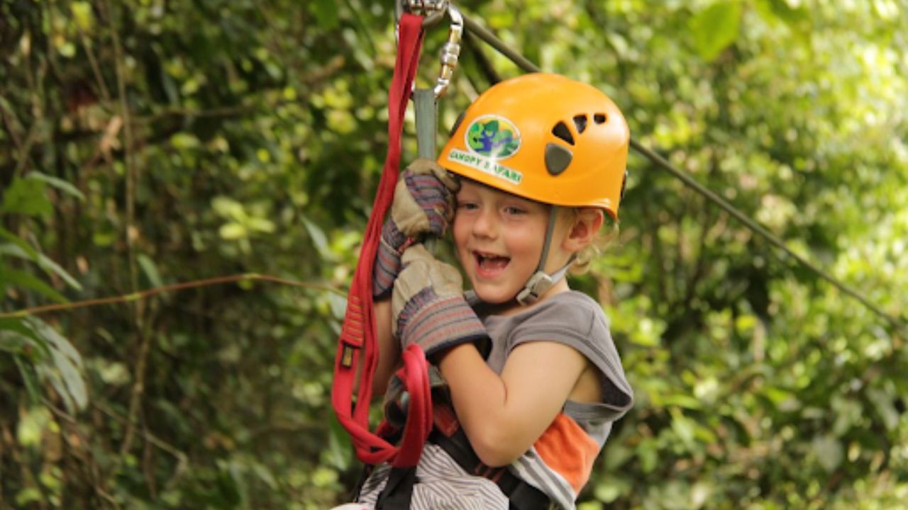 A small girl enjoying a zipline ride through a lush forest canopy.