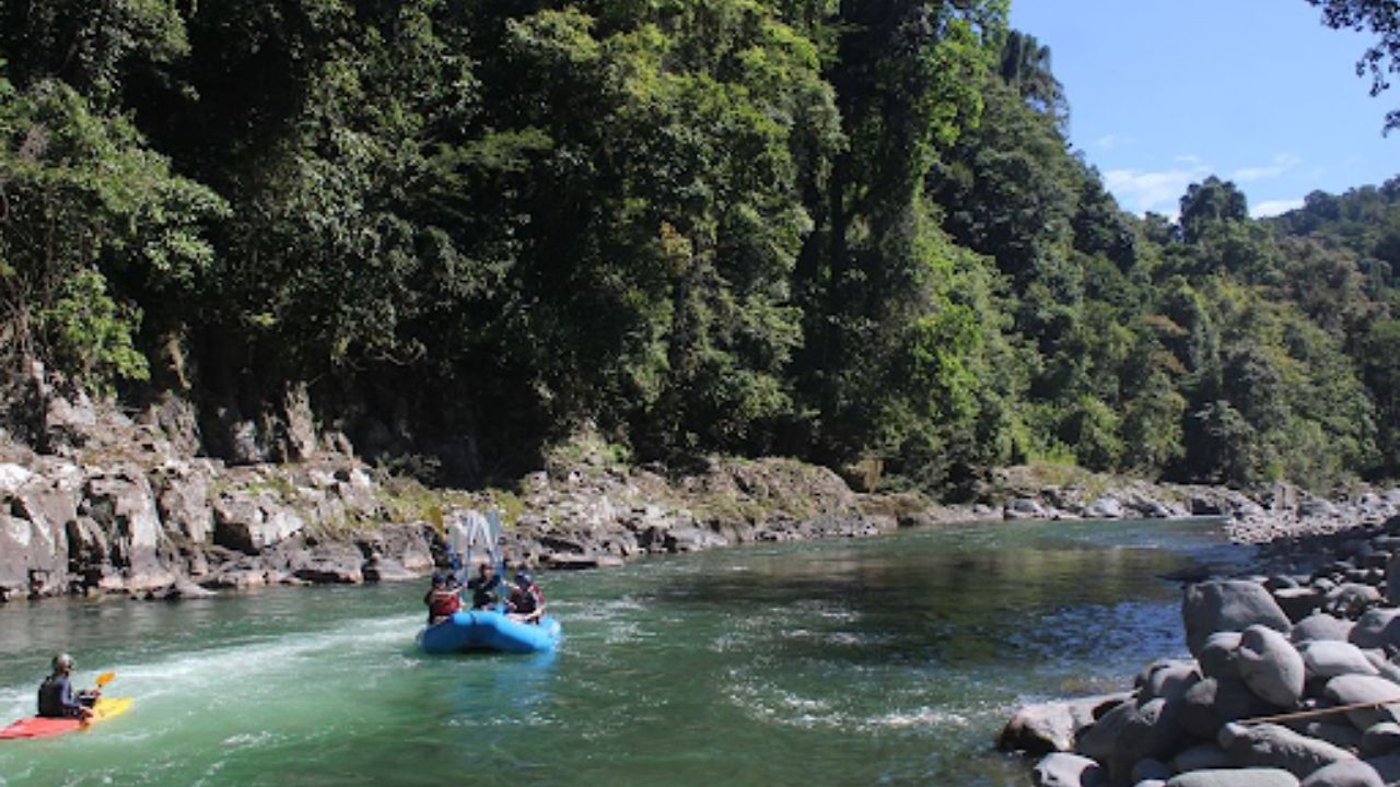 White water rafting group floating down a calm jungle and rocky riverbanks in Costa Rica.